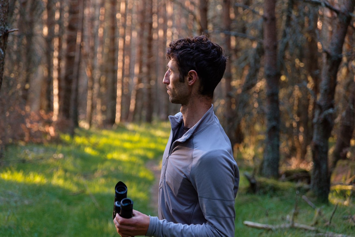 A person stands on the Abergeldie Estate, gazing into the warm light of the setting sun. Behind them, dense forest hides the rolling hills beyond. A landscape once only seen from afar through binoculars.