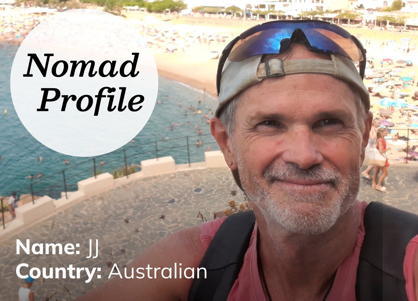 A white man wears a backwards baseball cap and sunglasses on his head. He has a light grey beard and wry smile. He’s taking a selfie from a look-out point with a stretch of beach in the background.