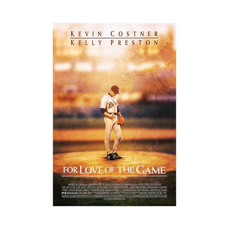 May include: A movie poster for the film 'For Love of the Game' starring Kevin Costner and Kelly Preston. The poster features a baseball player in a white uniform and a baseball cap, standing on a baseball field. The background is a blurred image of a baseball stadium. The title of the film is in large, white letters at the bottom of the poster.