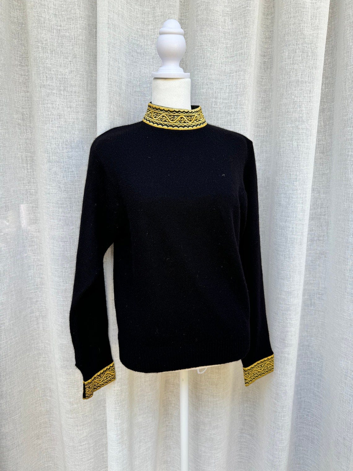 May include: A black mock neck sweater with gold trim around the neck and cuffs.
