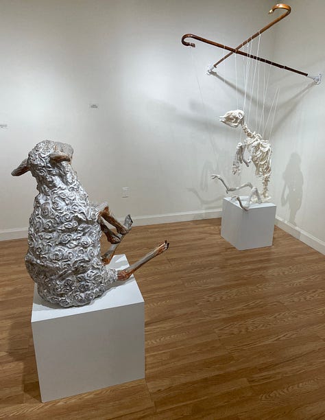 Installation views of a gallery with several artworks depicting sheep. All works are made of ceramic with fiber attachments connecting them together.