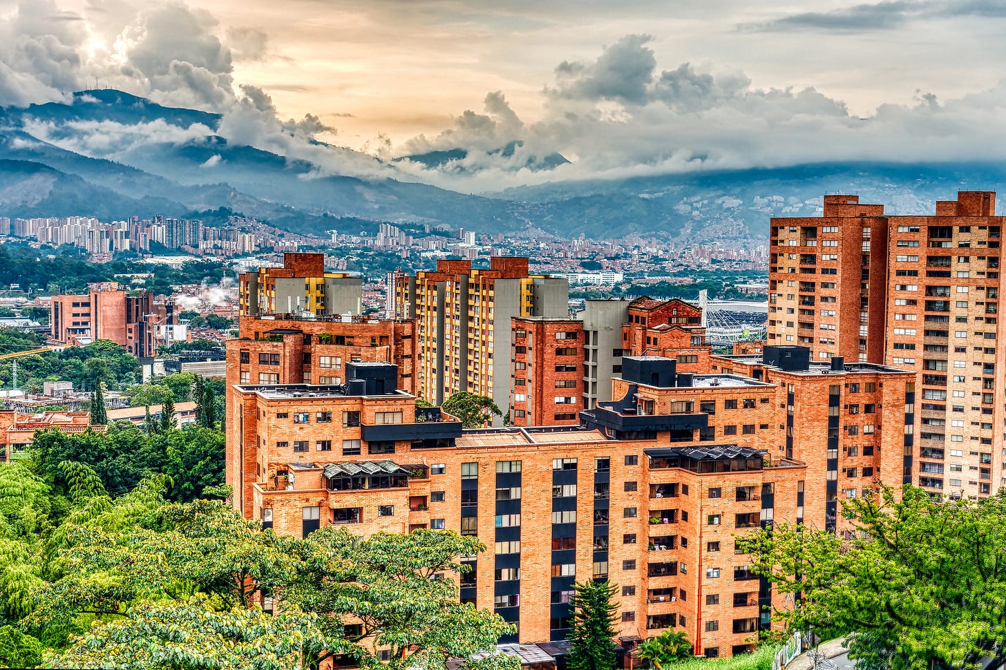 Red-brick residential apartment towers rising against the green Andean mountains in Medellín, Colombia.