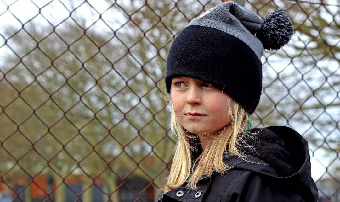 woman in black knit cap and black coat standing near gray metal fence during daytime