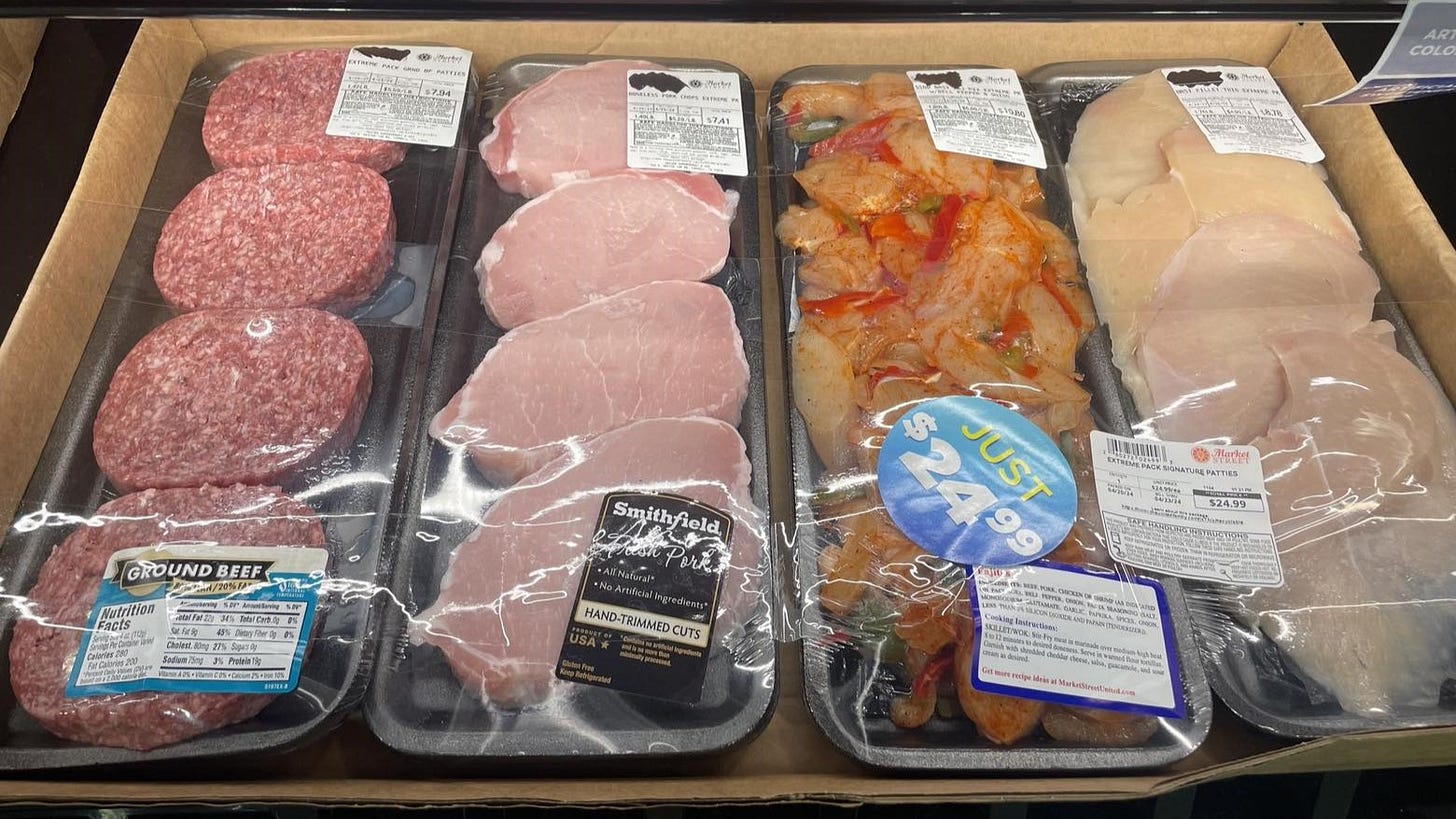 A tray of four burger patties, four pork chops, four chicken breasts, and a comparable amount of chicken prepared for fajitas