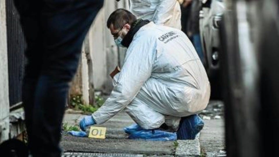 Un operatore della scientifica dei Carabinieri, con tuta protettiva e mascherina, effettua i rilievi su un marciapiede accanto a un reperto contrassegnato dal numero 10.