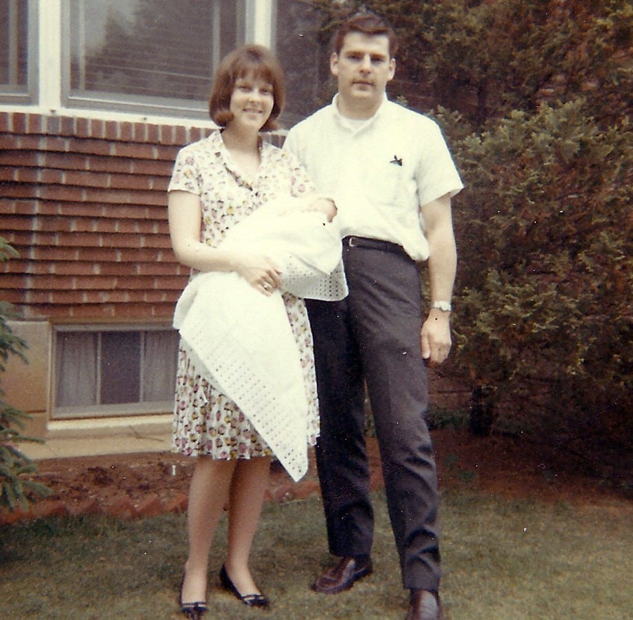 Young couple poses with their newborn in front of their home on the baby's Christening Day Young couple poses with their newborn in front of their home on the baby's Christening Day