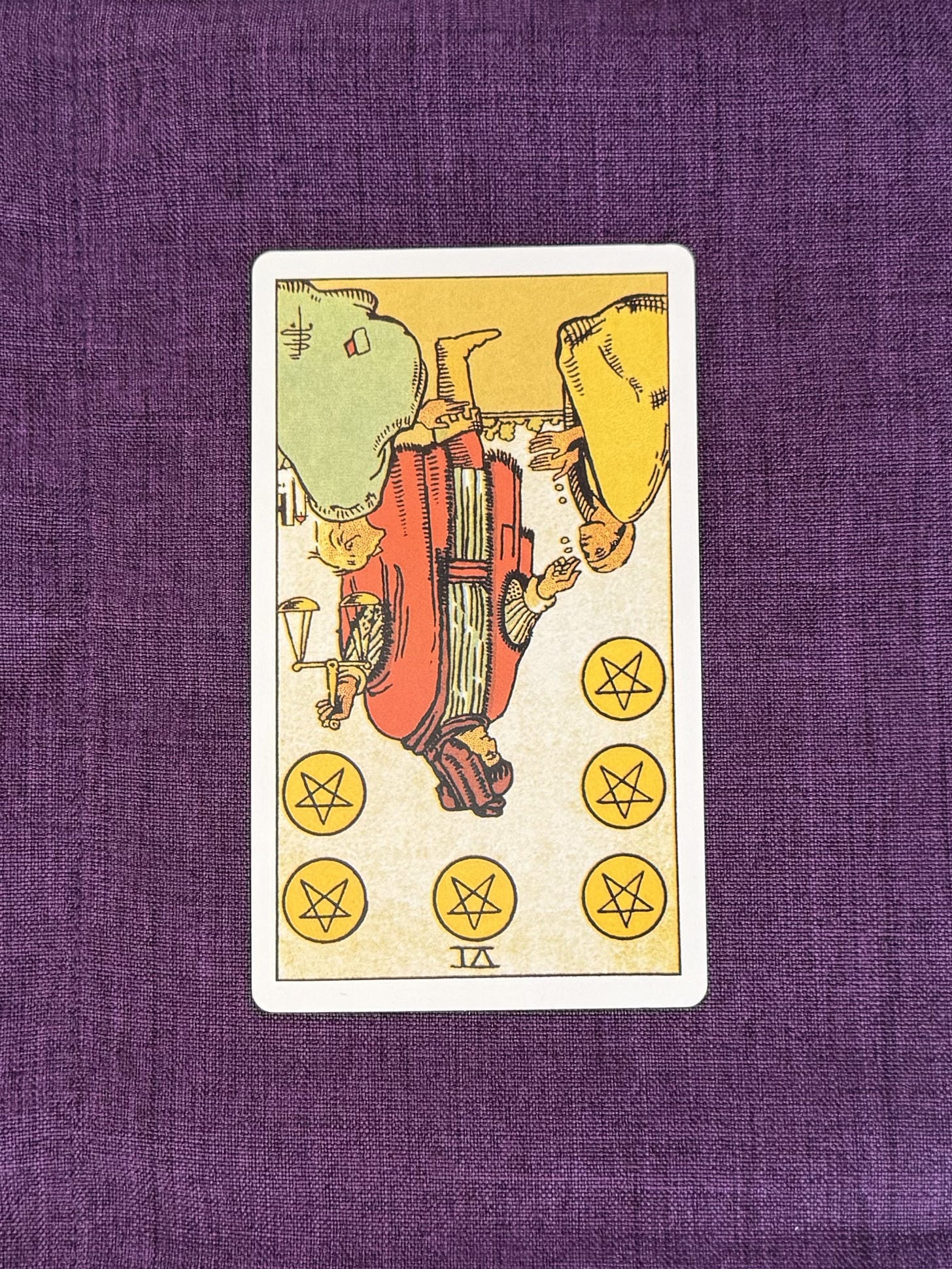 A standing figure wears a long robe and holds a balance scale in one hand while extending the other hand toward two kneeling figures. The standing figure offers golden coins to the figures below. Six golden coins are arranged in the upper part of the image, with three on each side. Buildings are visible in the background beneath a clear sky.