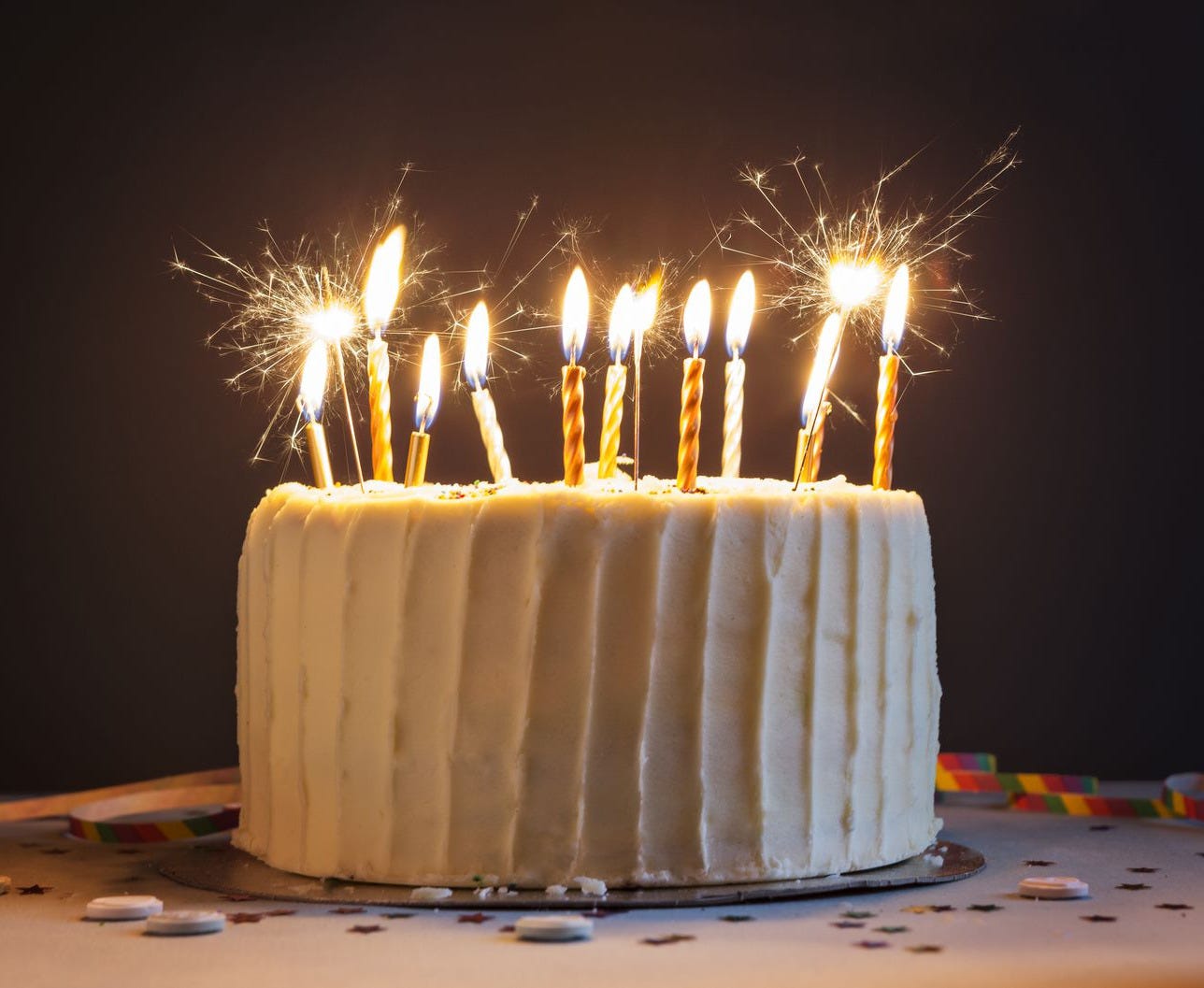 image of a white birthday cake against a dark backdrop with sparkling lit candles on top