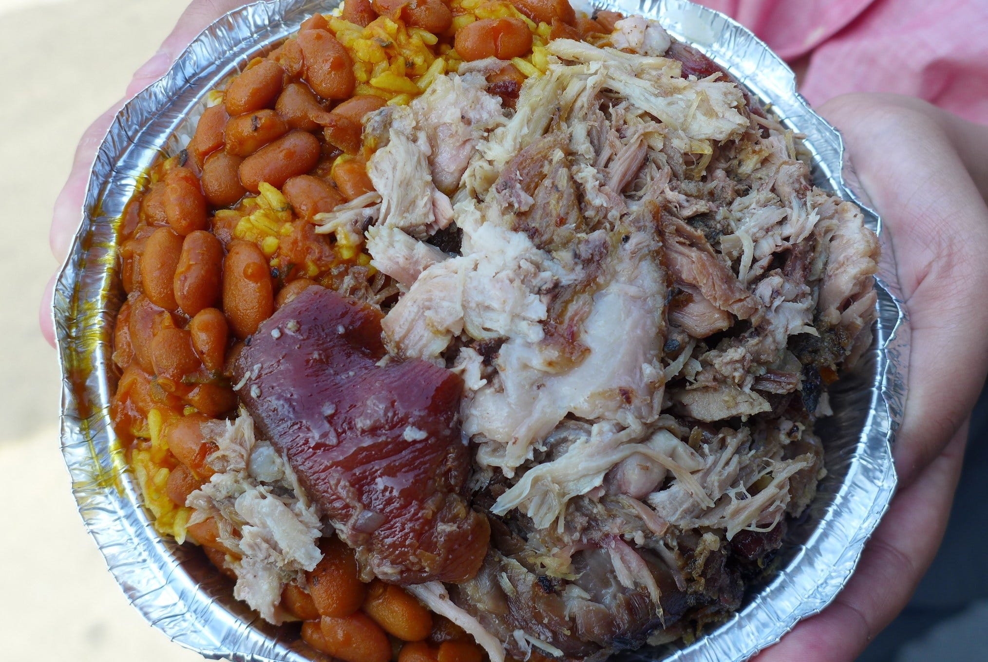 A round aluminum container of pork and brown skin, brown beans, and yellowish rice packed in tight.