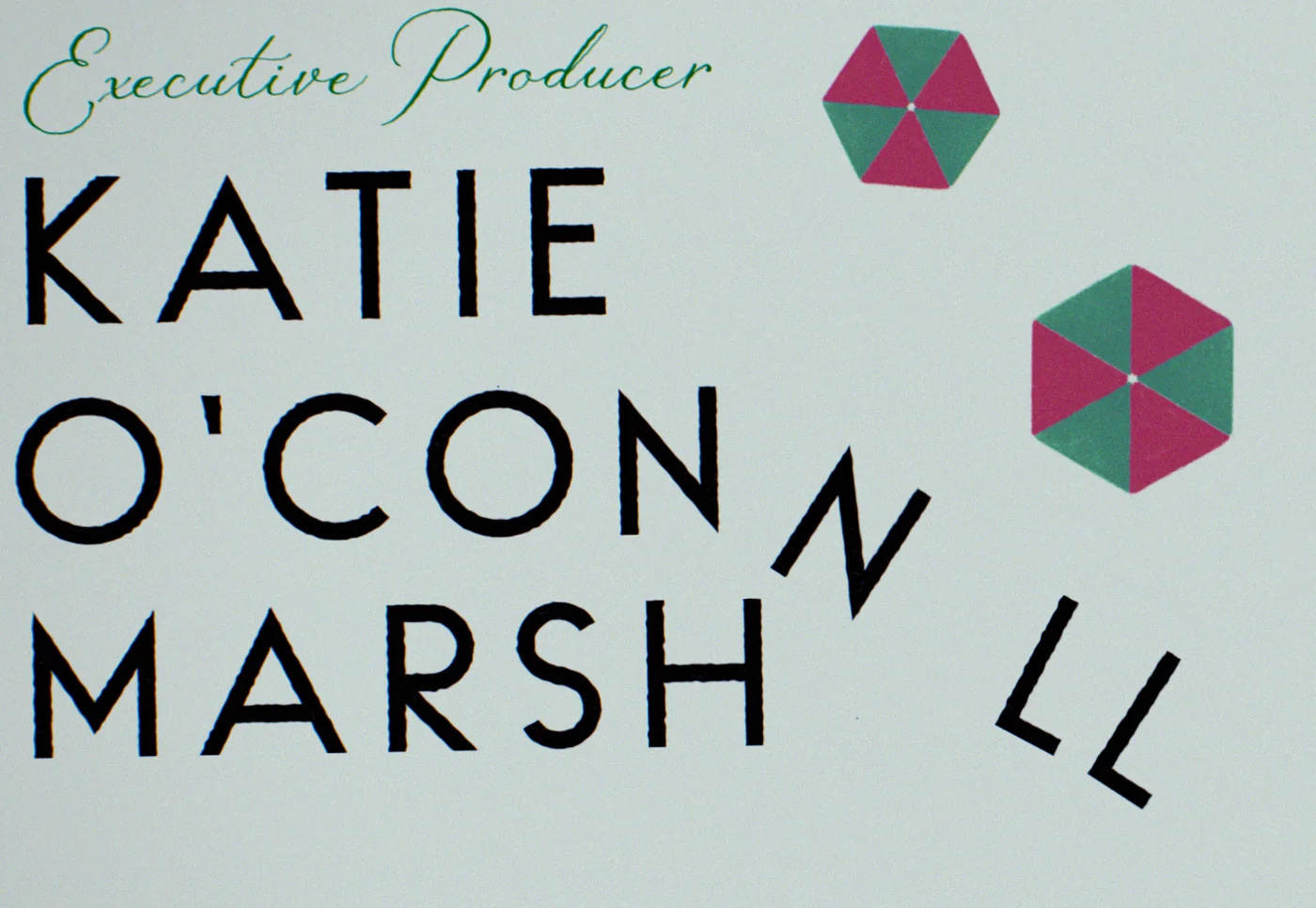 Texto, escrito à mão: Produtora Executiva. Abaixo, em destaque, o nome de Katie O'Connell Marsh em fonte grande é derrubado por pequenos guarda-chuvas como os de drinks. Texto, escrito à mão: Produtora Executiva. Abaixo, em destaque, o nome de Katie O'Connell Marsh em fonte grande é derrubado por pequenos guarda-chuvas como os de drinks.