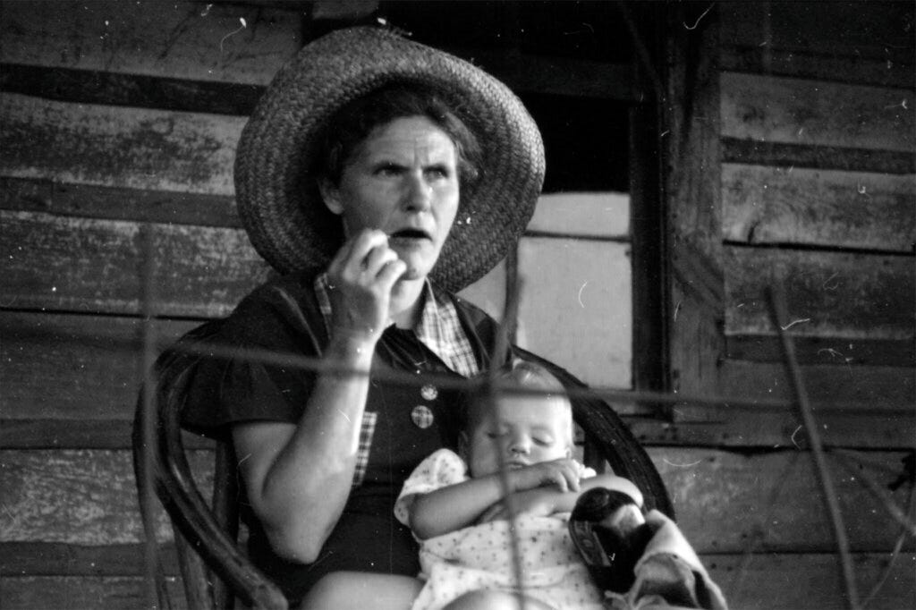 Myrtle Lawrence sits on her porch holding a sleeping baby | Flickr