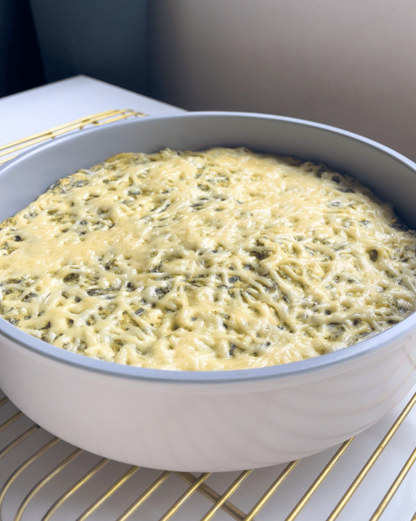 vegan spinach artichoke dip in a round grey pan on wire cooling rack