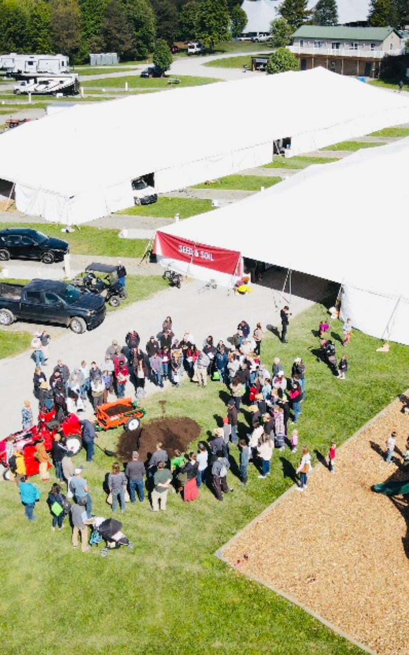 Aerial view of a crowd gathered by large white event tents at an outdoor homesteading summit. Aerial view of a crowd gathered by large white event tents at an outdoor homesteading summit.