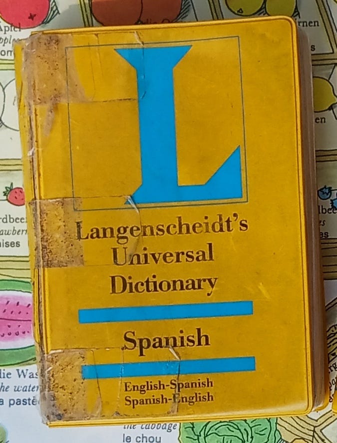 Battered yellow pocket Spanish dictionary held together with tape, with smudges on the cover. It's been much loved but it still works!.