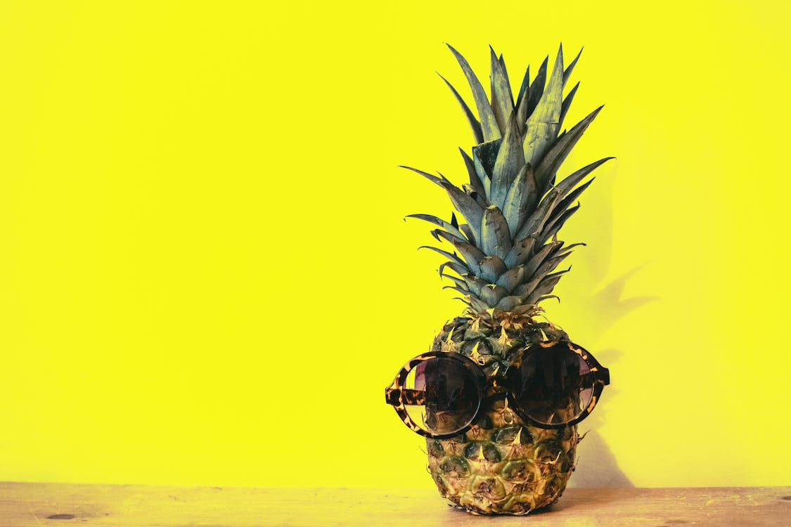 Free Green Pineapple Fruit With Brown Framed Sunglasses Beside Yellow Surface Stock Photo
