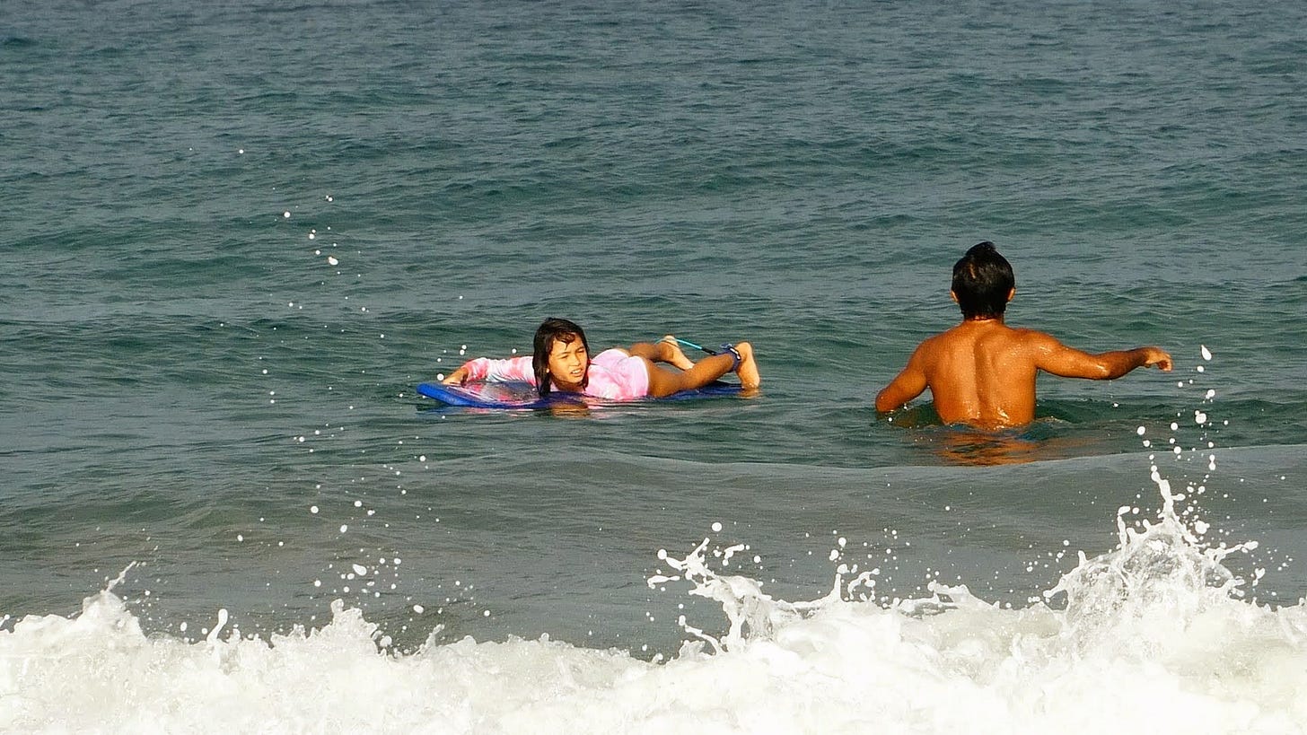 Little girl lying on surfboard in ocean, with foamy waves crashing in front of her, at Playa Grande, Guanacaste.