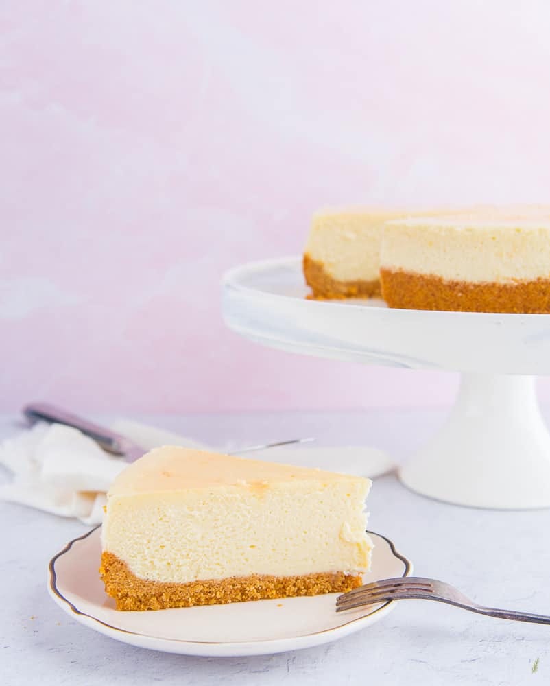 A portrait image of a slice of Classic Cheesecake with Graham Cracker Crust on a white plate A portrait image of a slice of Classic Cheesecake with Graham Cracker Crust on a white plate