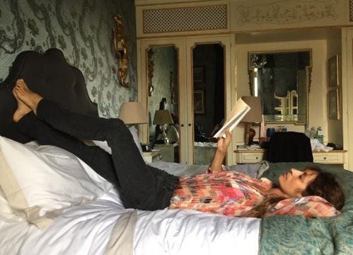 This may contain: a woman laying on top of a bed with a book in her hand while reading