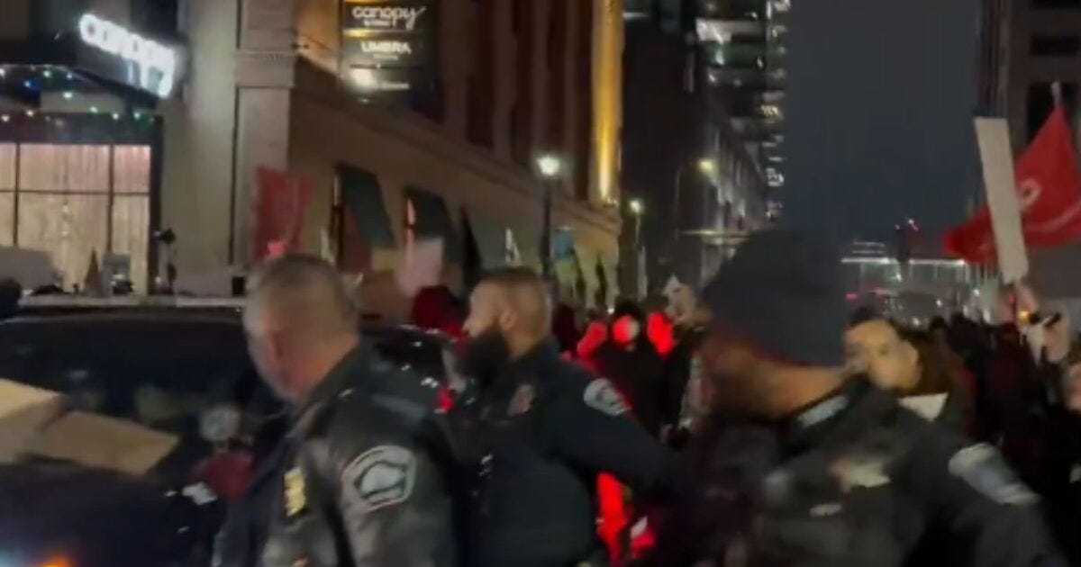 Police officers manage a large protest with demonstrators holding signs in a city street at night.