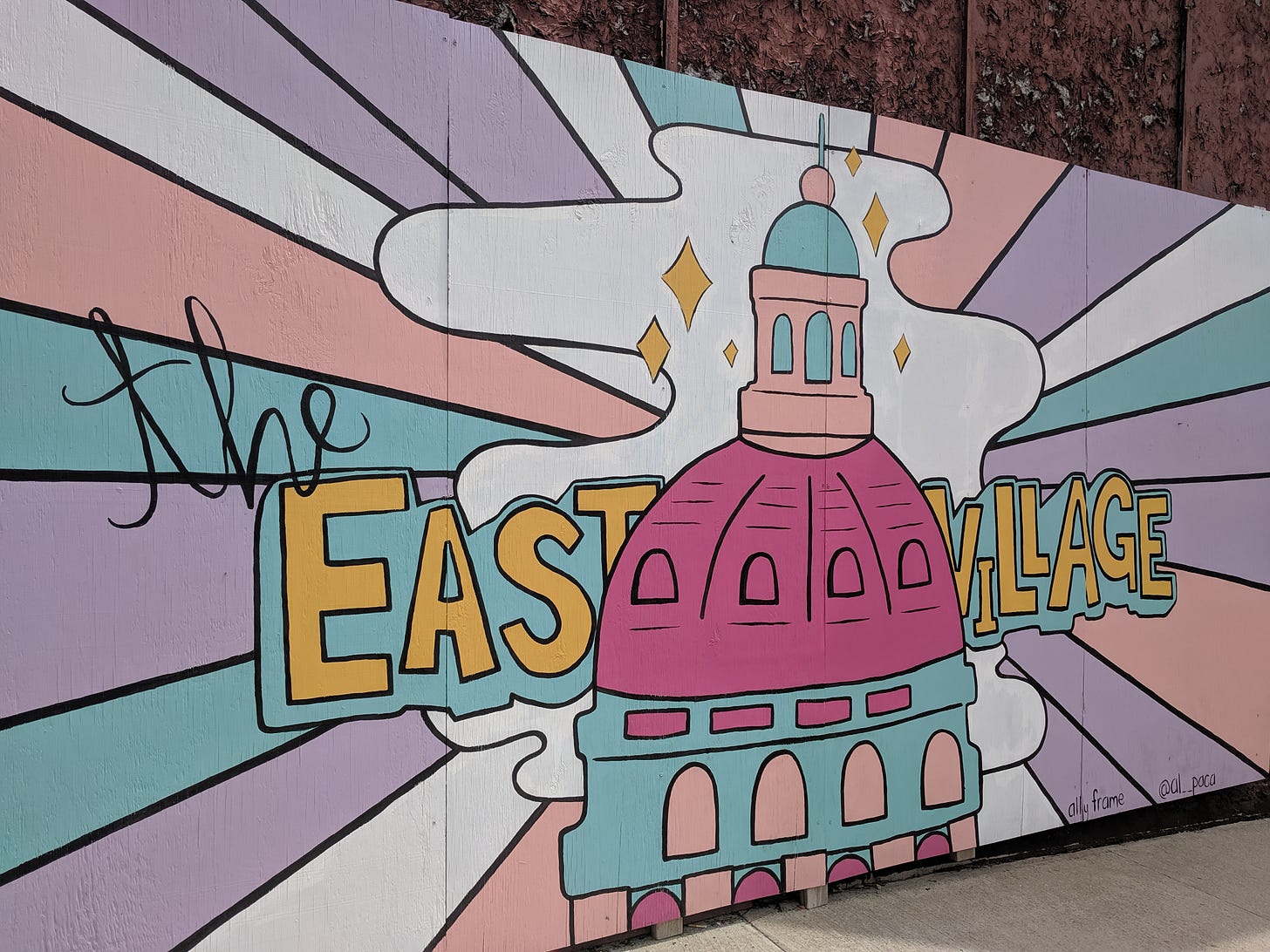 A painted mural of the Capitol Building with pastel light rays emanating from it with the words "the East Village" overlayed in script and bold