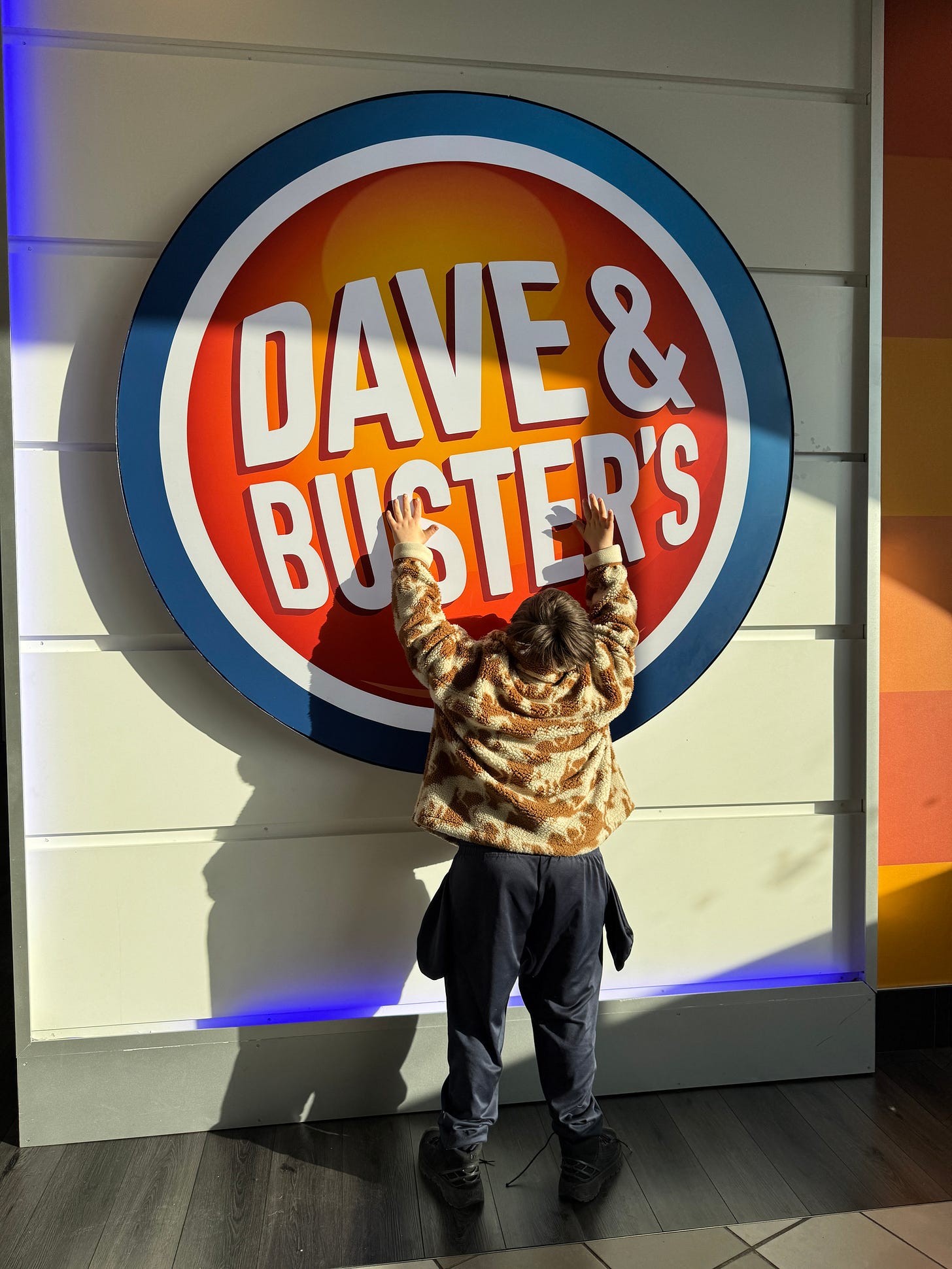 A boy holds both hands up to touch a large Dave and Busters wall logo.