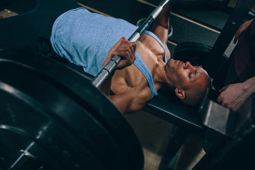 Man Bench Pressing in the gym with a spotter.