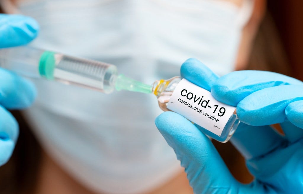 A person in medical gloves fills a syringe from a vial labeled "covid-19 coronavirus vaccine."