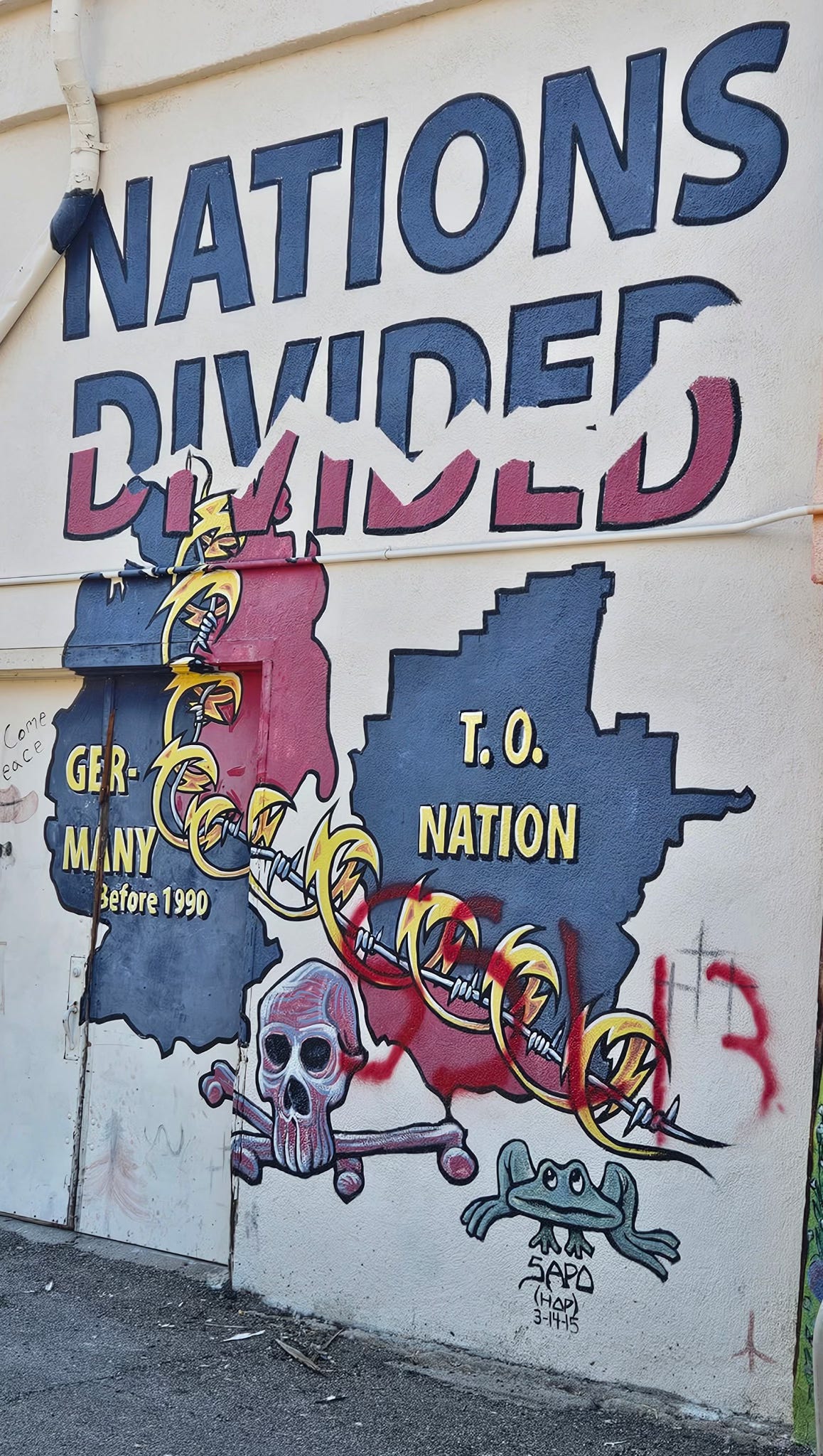 A mural with the words "Nations Divided" split in two and, below that, a drawing of pre-unification Germany and the Tohono O’odham Nation, both split in two by a coil of barbed wire.