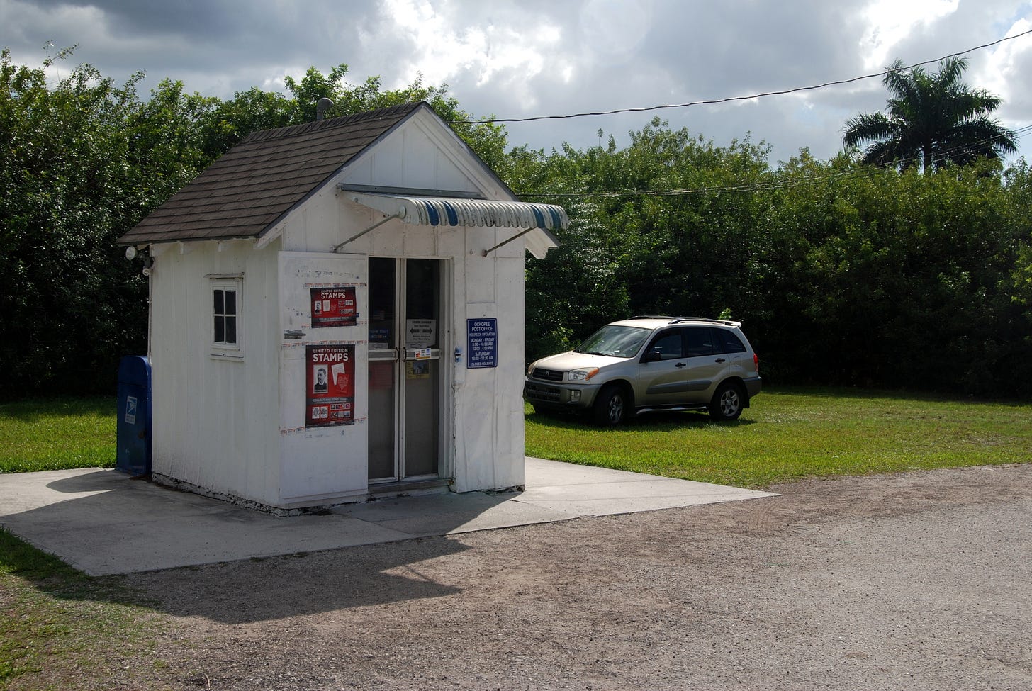 Tiny shack with Post Office signage, car parked next to it Tiny shack with Post Office signage, car parked next to it