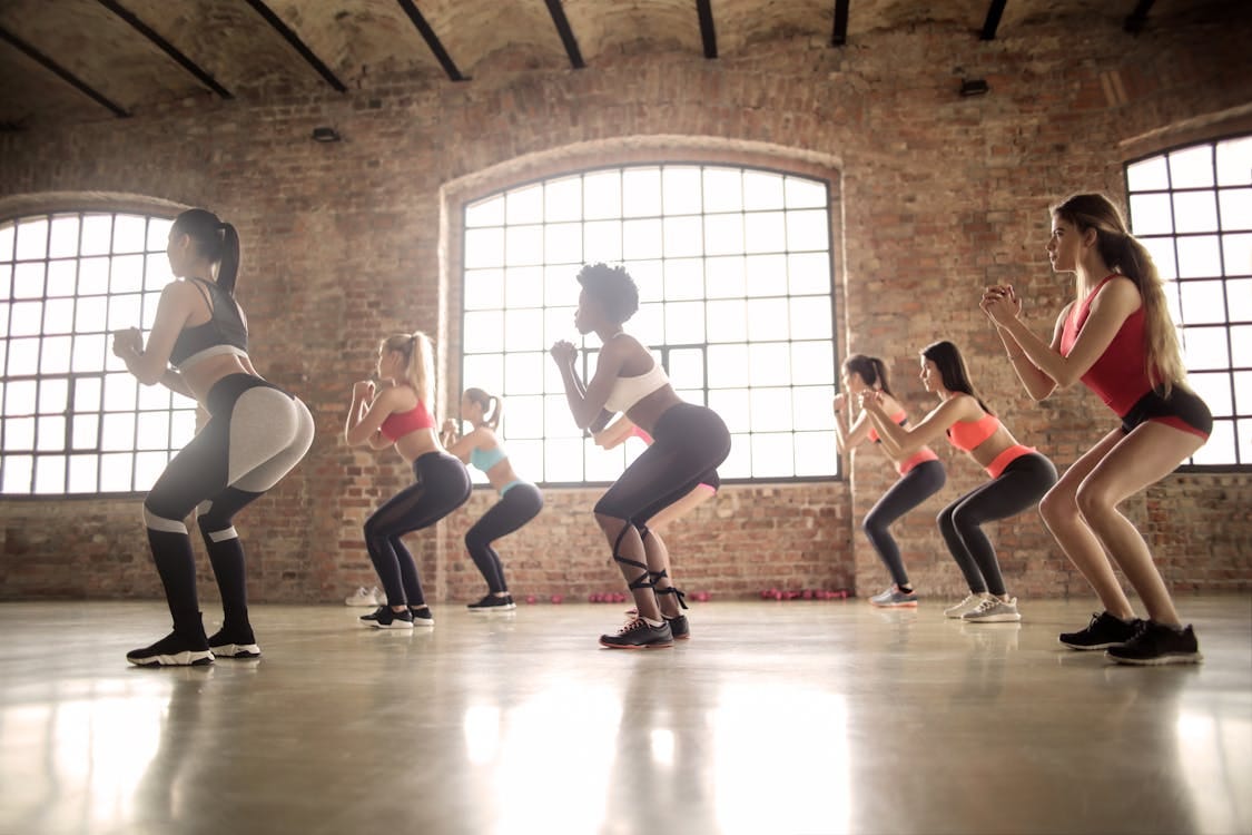 Free Women participating in a group fitness class performing squats in an industrial-style studio. Stock Photo Free Women participating in a group fitness class performing squats in an industrial-style studio. Stock Photo