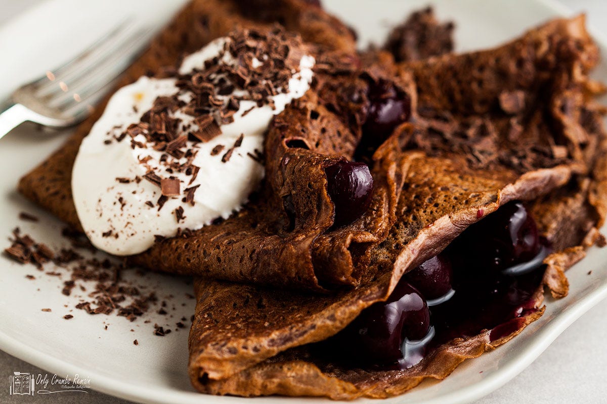 black forest pancakes on plate topped with cream with a fork to the side.