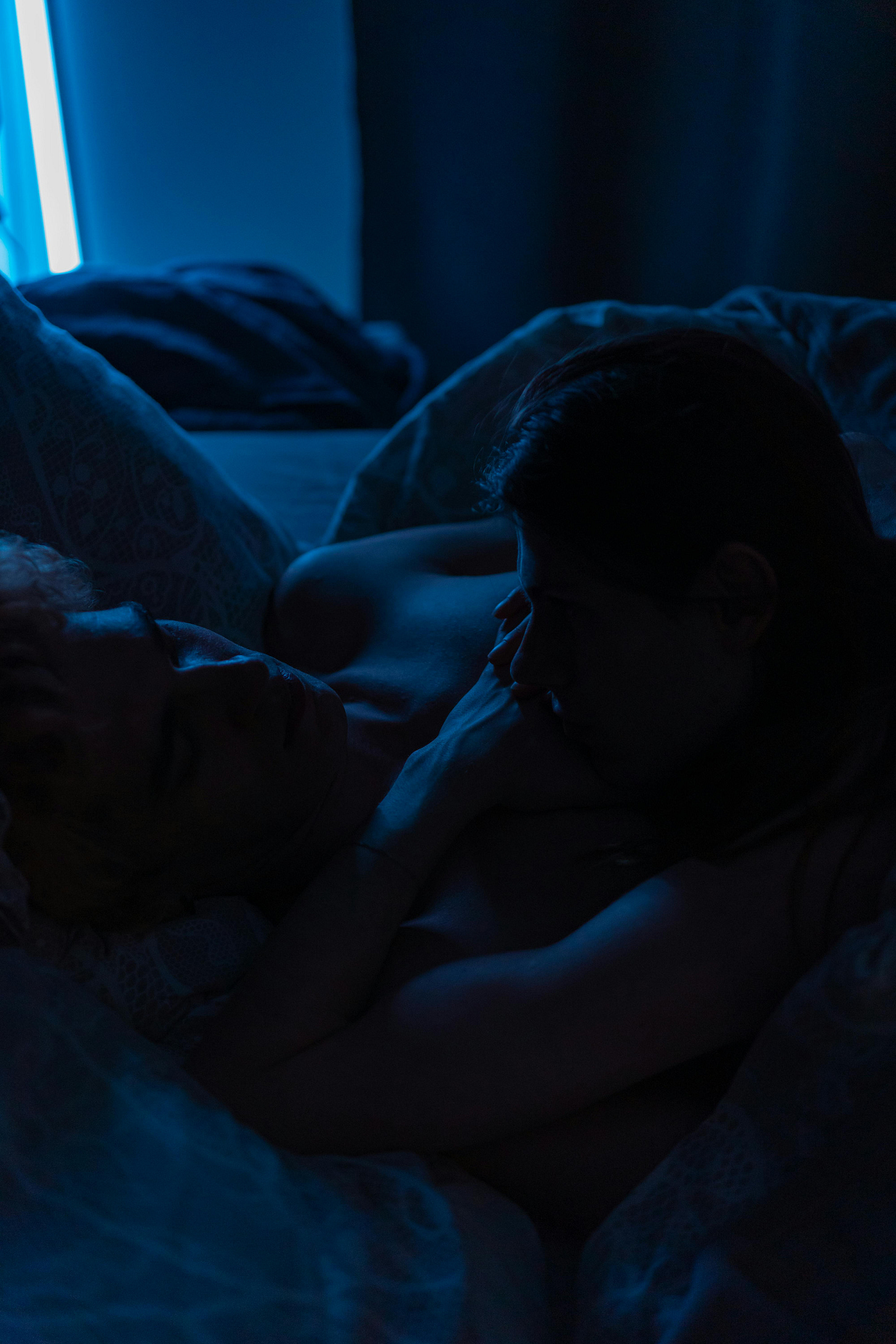 Free A romantic embrace between two adults in a dark, ambient bedroom setting. Perfect for themes of love and intimacy. Stock Photo