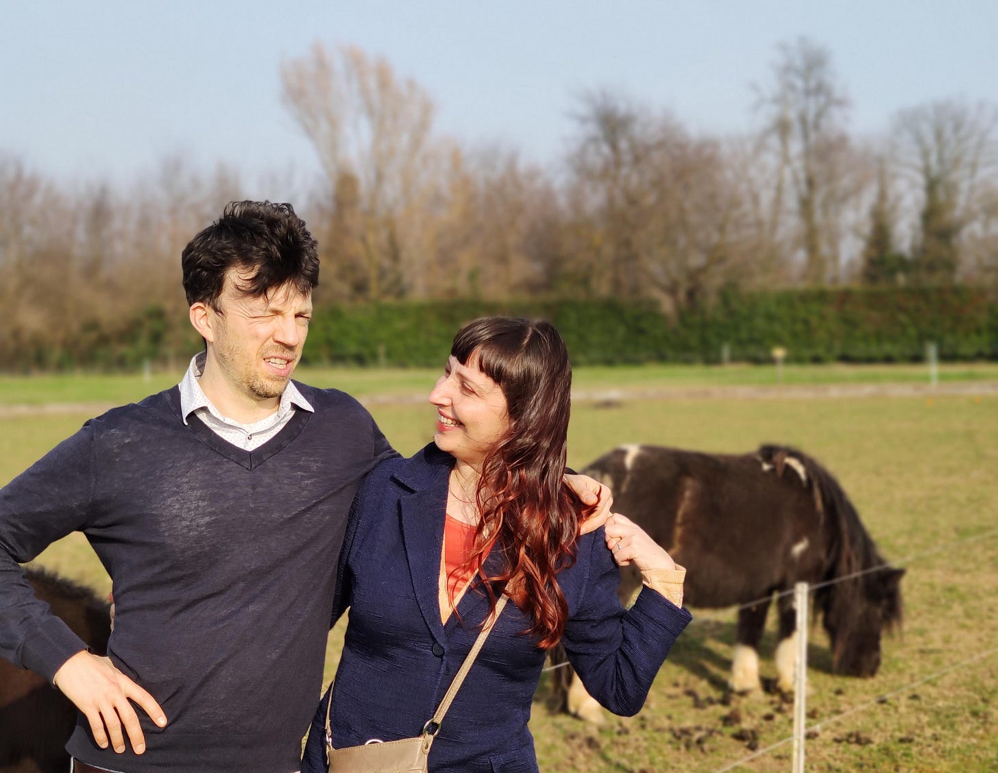 Un uomo e una donna sui 40 si guardano. Federico sta facendo una smorfia, Elena sorride. Sullo sfondo, un pony e un ampio prato verde. Un uomo e una donna sui 40 si guardano. Federico sta facendo una smorfia, Elena sorride. Sullo sfondo, un pony e un ampio prato verde.