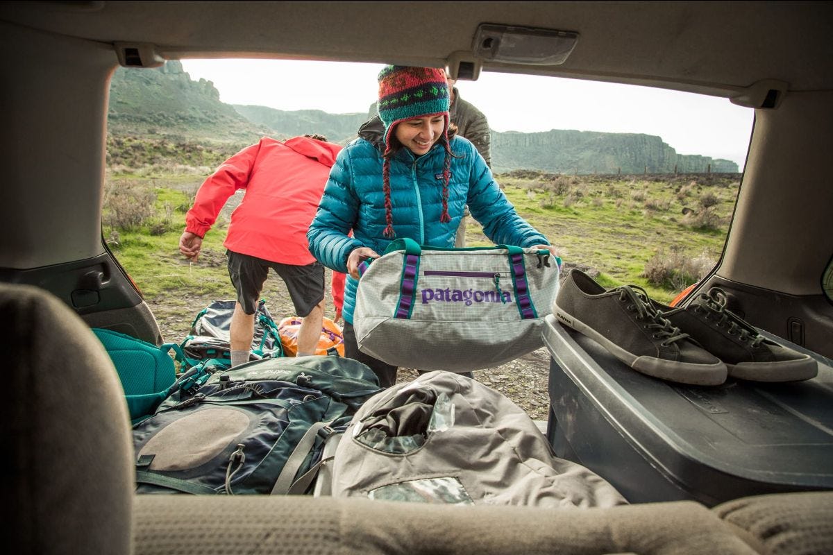 a woman pulls a patagonia black hole duffet out of the trunk of an suv