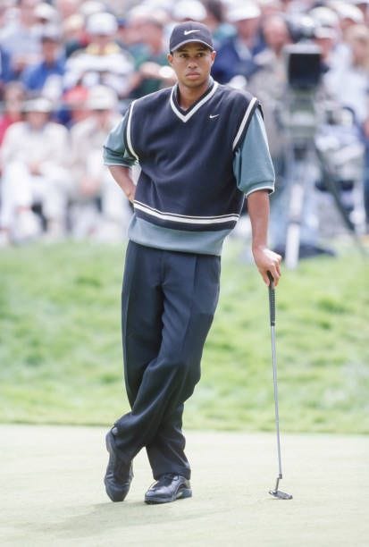 This may contain: tiger woods walking on the green with his golf club in hand and people watching from the stands behind him This may contain: tiger woods walking on the green with his golf club in hand and people watching from the stands behind him