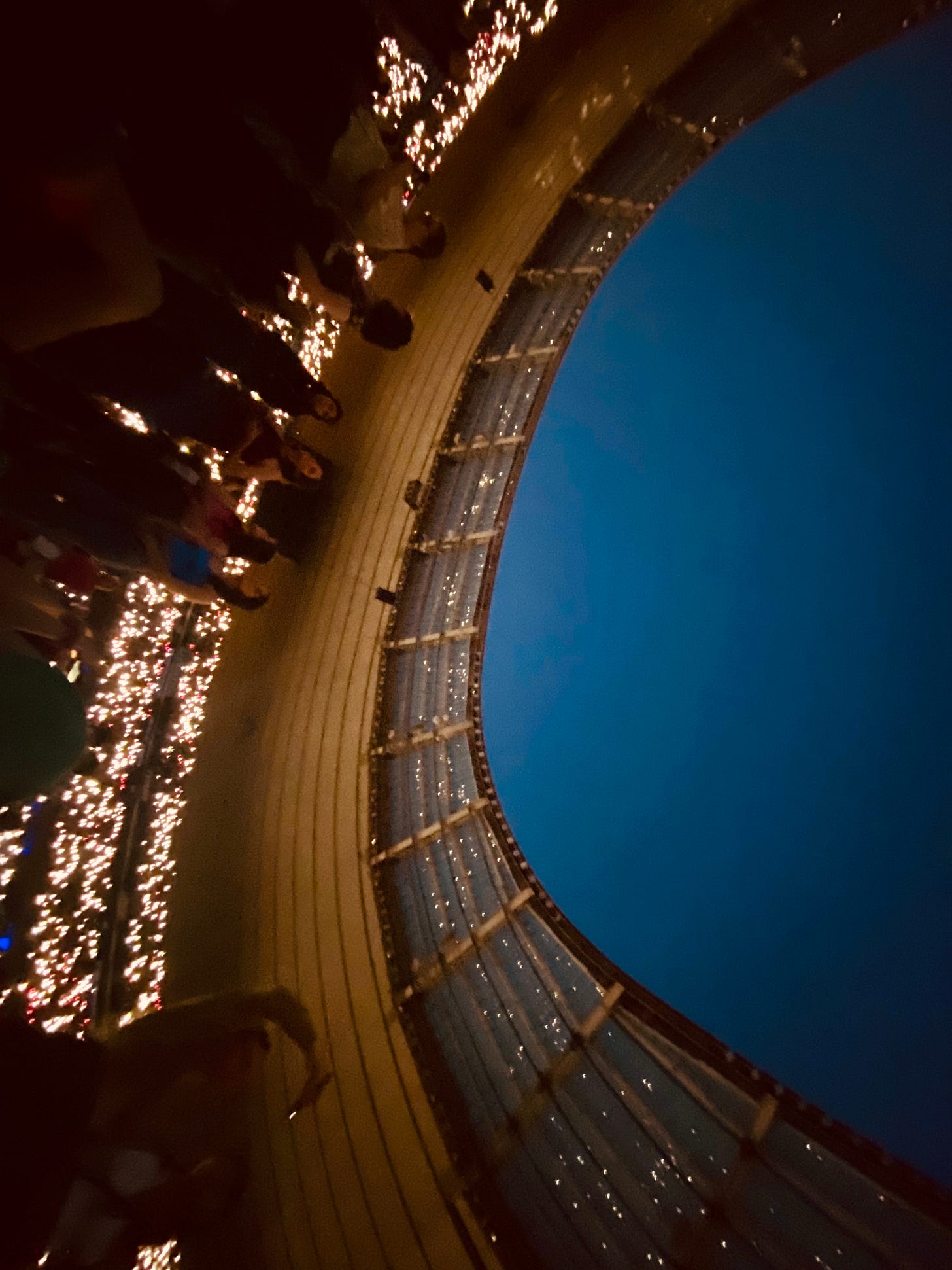 The blue night sky above the stadium and the lights from the fans' phones in the stands and reflected in the partial roof