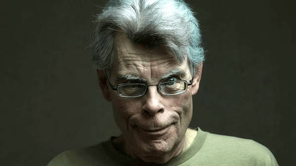 A close-up portrait of a middle-aged man with white hair, glasses, and an expressive smile, wearing a green shirt, set against a dark background. A close-up portrait of a middle-aged man with white hair, glasses, and an expressive smile, wearing a green shirt, set against a dark background.