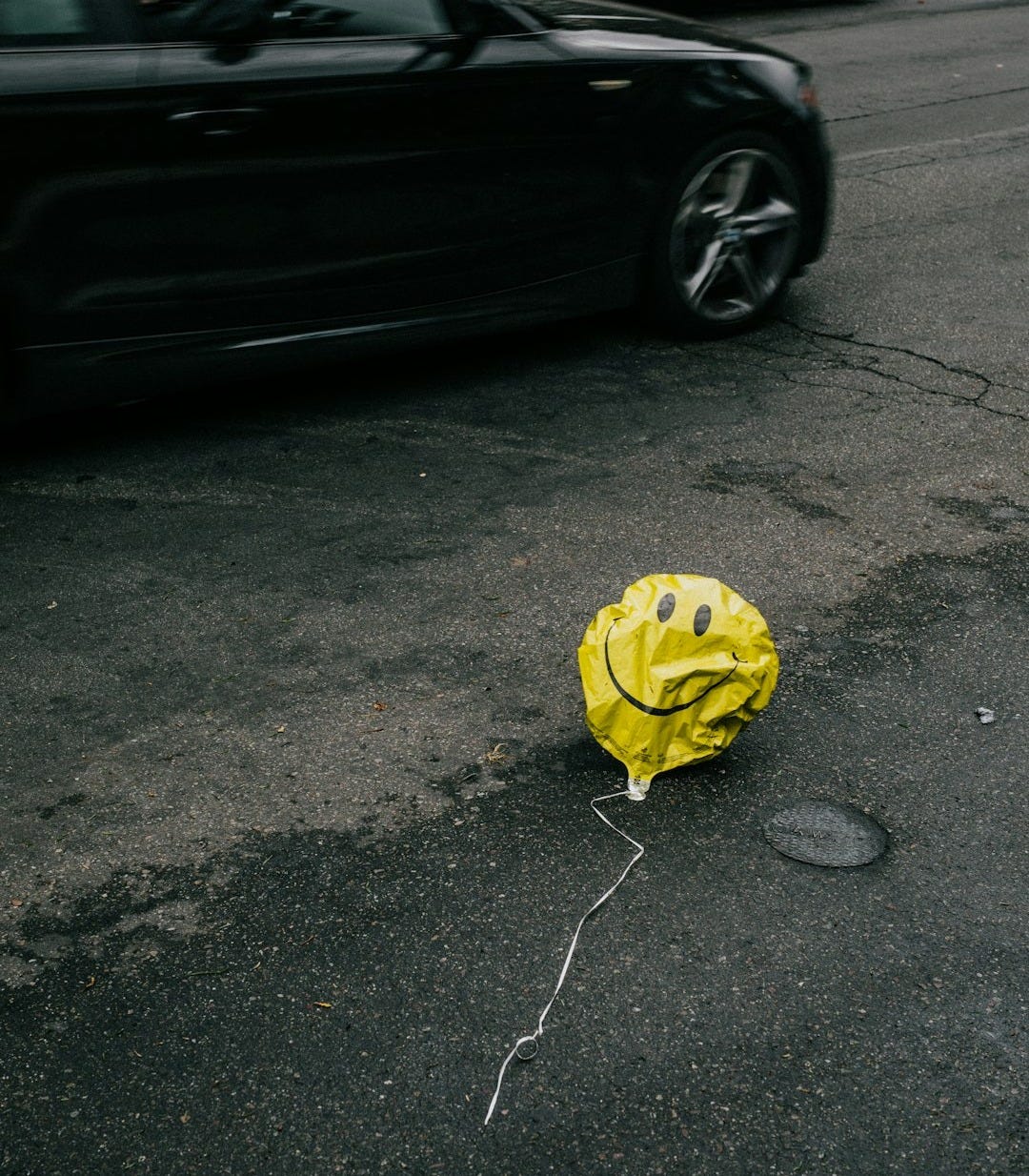 smiling emoji balloon beside black car during daytime