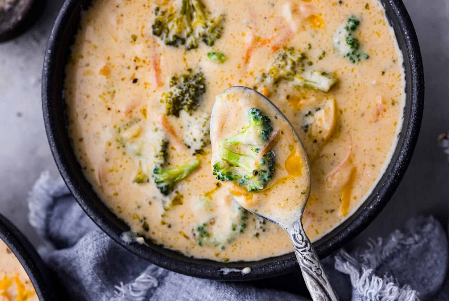 A close up of the broccoli cheese soup in a bowl with a spoon scooping some out. 