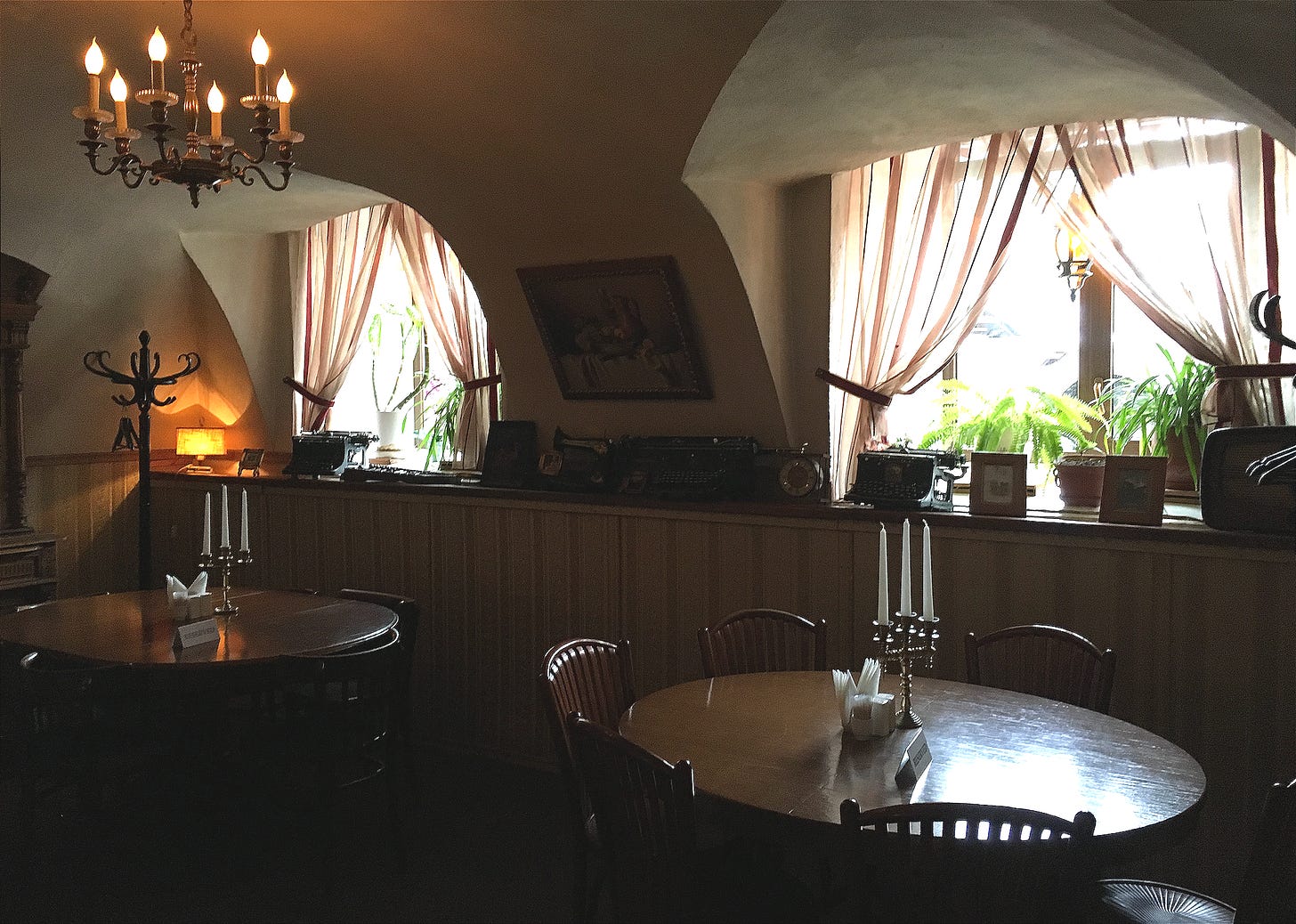 Interior of The Idiot restaurant showing vaulted archways, wooden tables with candles, hanging chandelier, striped curtains on arched windows, and warm atmospheric lighting.