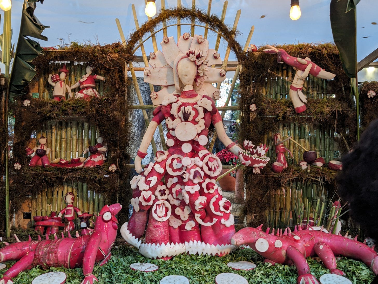 A woman with a red dress with flowers is roughly carved out of red and white radishes. There are two red lizards by her side.