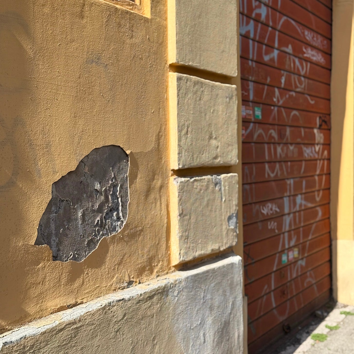 A weathered Roman wall with chipped plaster beside a wooden garage door covered in graffiti—capturing texture, decay, and layered urban history.