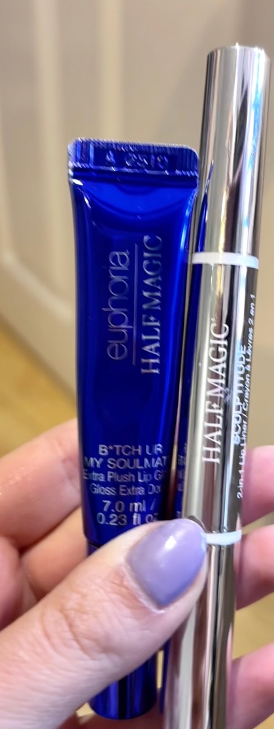 A close-up shot of the Half Magic ‘BTCH UR MY SOULMATE’ lip gloss and the dual-ended Sculptitude lip liner held in a hand with lilac-painted nails.