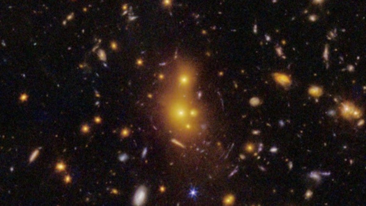 A dense galaxy cluster, possibly the most distant lens cluster, features bright yellow-white central galaxies surrounded by numerous smaller galaxies against a dark space background—a scene revealing the surprises of dark matter. A dense galaxy cluster, possibly the most distant lens cluster, features bright yellow-white central galaxies surrounded by numerous smaller galaxies against a dark space background—a scene revealing the surprises of dark matter.
