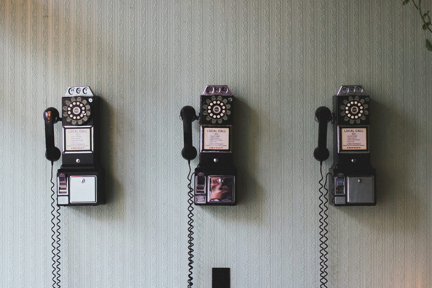 A photo of three rotary pay phones on a wall.