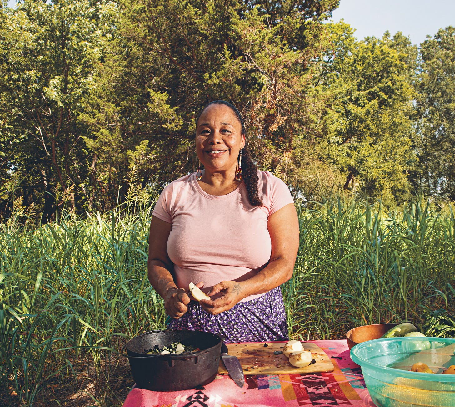 Chef Crystal Wahpepah standing in a field preparing food in a cast iron pot