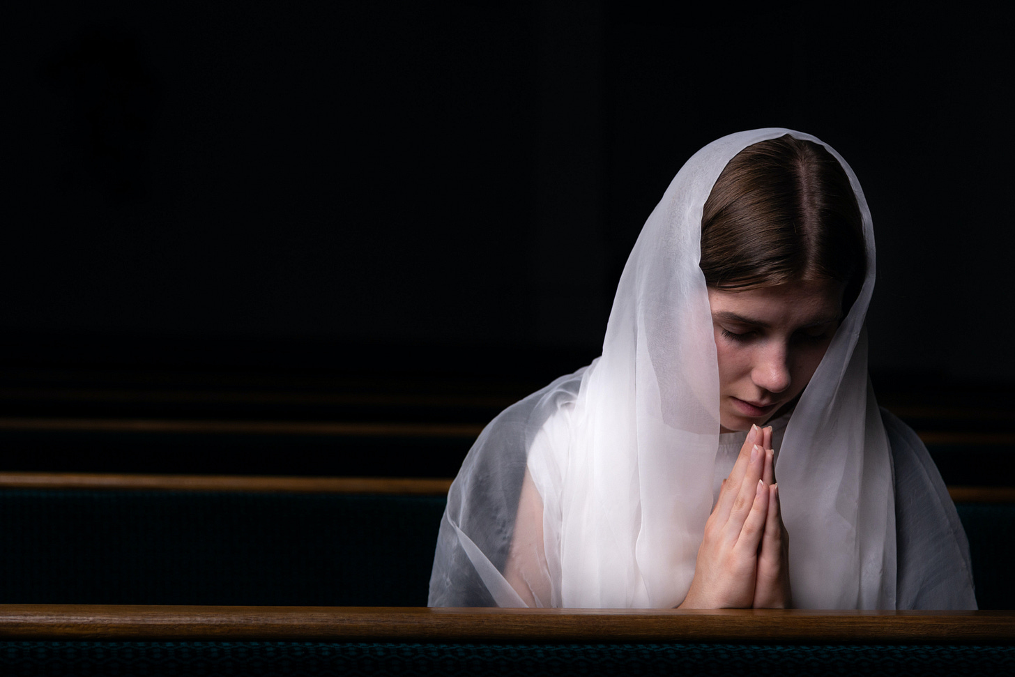 A woman wearing a white veil prays in a church. A woman wearing a white veil prays in a church.