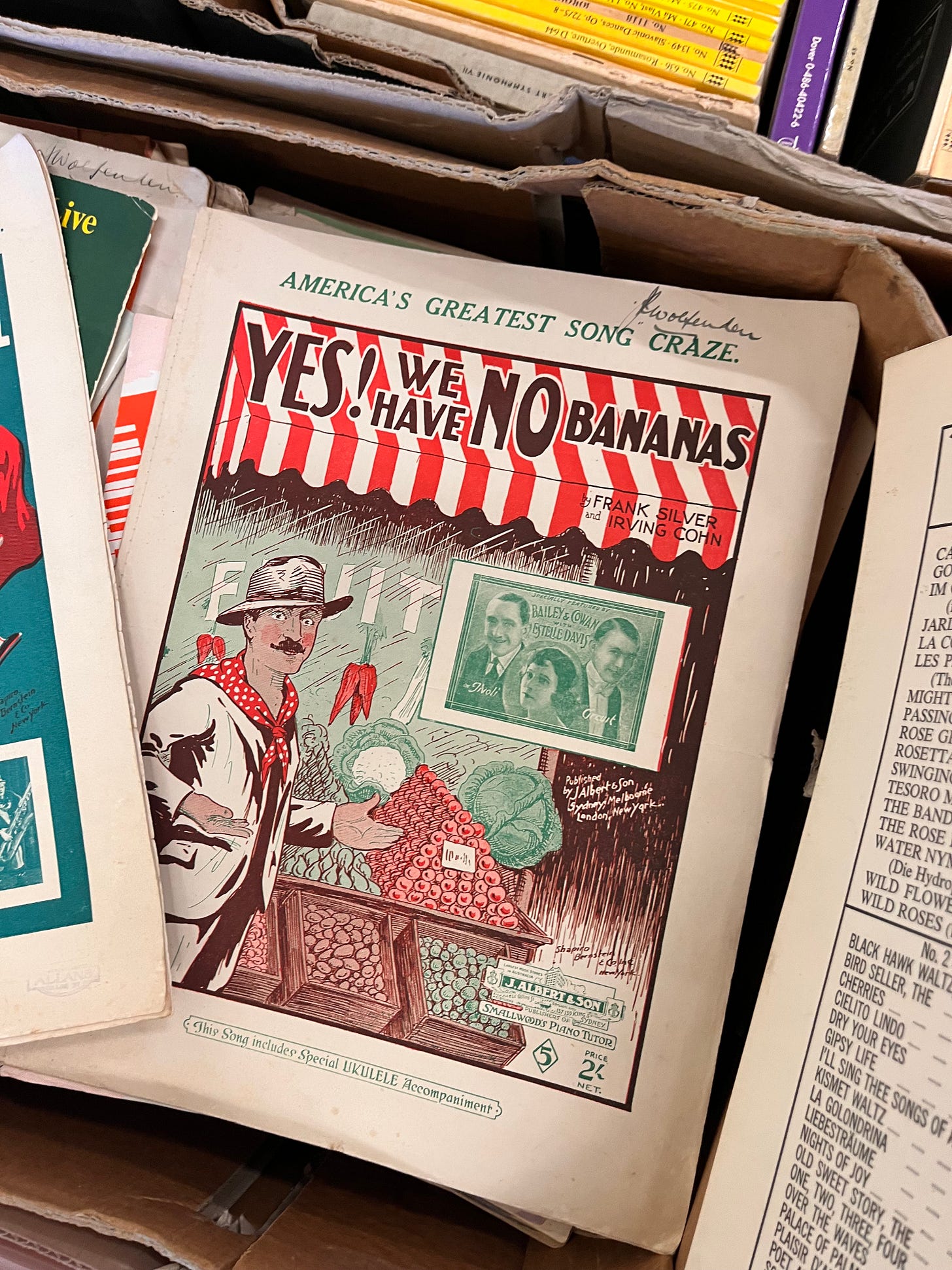 A piece of sheet music for 'Yes! We have no bananas", with a red and green illustration of a man in front of a fruit shop