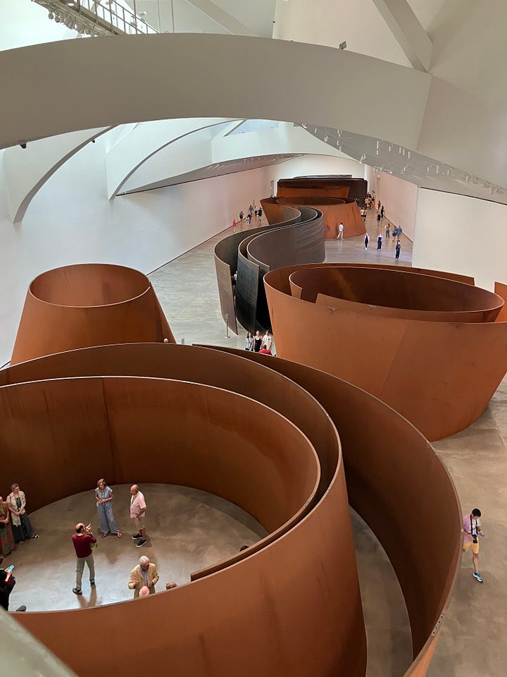 a view of spiral metal sculptures from above, with people around and within them, and a view through splintered glass of an elevator shaft