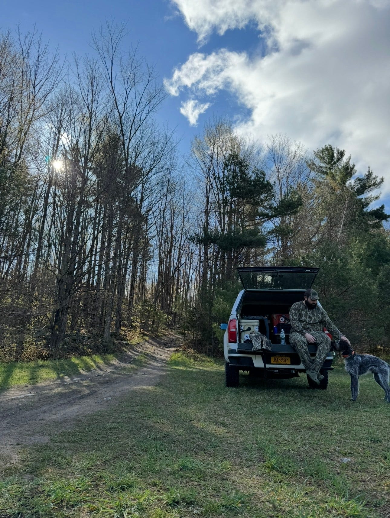 A turkey hunter resting on the tailgate with his bird dog.